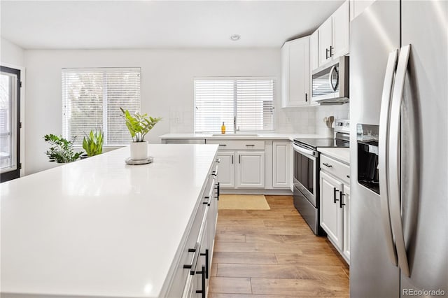 kitchen with appliances with stainless steel finishes, backsplash, sink, light hardwood / wood-style flooring, and white cabinets