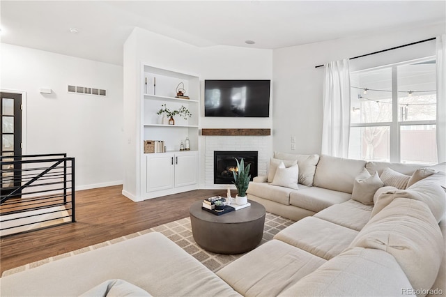 living room featuring hardwood / wood-style flooring, built in shelves, and a fireplace