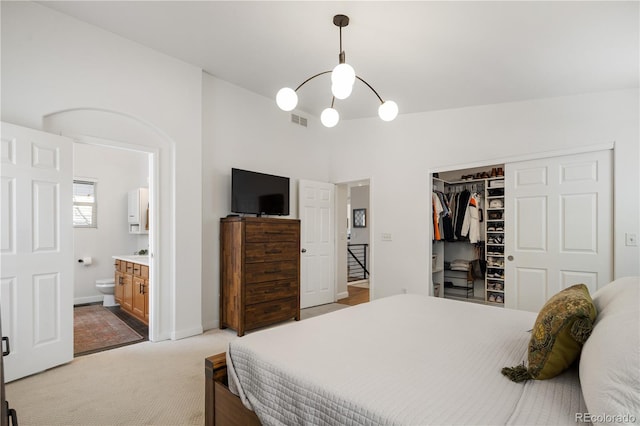 bedroom with ensuite bathroom, lofted ceiling, light carpet, and a closet