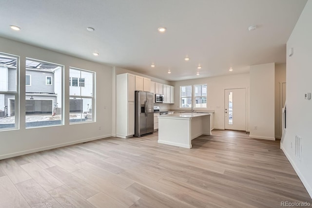 kitchen with light wood-type flooring, stainless steel appliances, white cabinetry, and a kitchen island