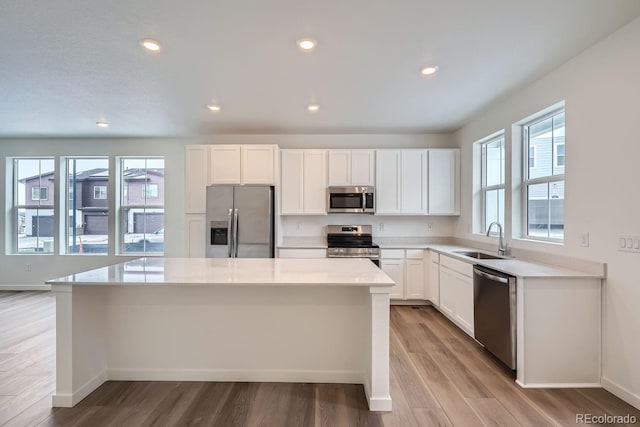 kitchen with appliances with stainless steel finishes, sink, light hardwood / wood-style flooring, a center island, and white cabinetry