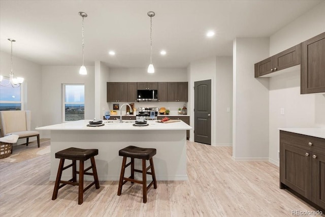 kitchen with appliances with stainless steel finishes, a kitchen island with sink, a breakfast bar, and light hardwood / wood-style flooring