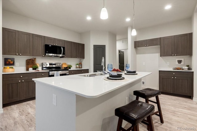 kitchen with a kitchen bar, sink, decorative light fixtures, stainless steel appliances, and a kitchen island with sink