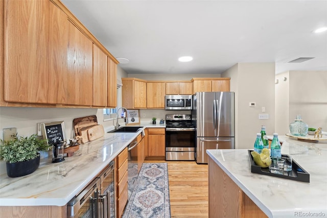 kitchen with sink, light wood-type flooring, appliances with stainless steel finishes, light stone counters, and beverage cooler