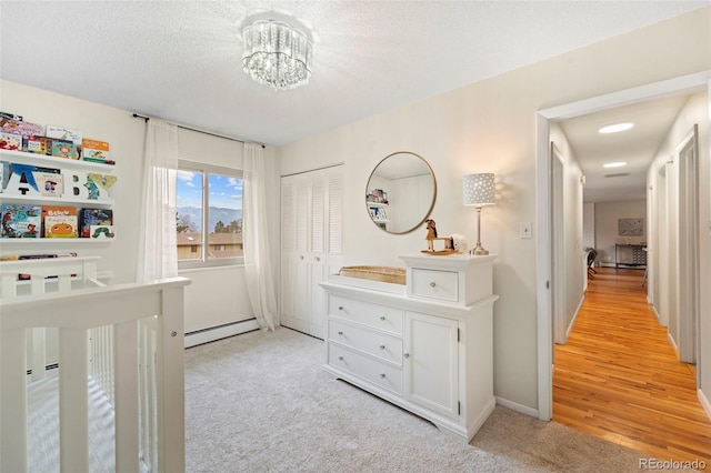 carpeted bedroom featuring a textured ceiling, a closet, baseboard heating, and a notable chandelier