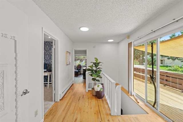 corridor featuring light wood-type flooring, a textured ceiling, and a baseboard radiator