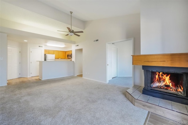 unfurnished living room with ceiling fan, vaulted ceiling, light carpet, and a tiled fireplace