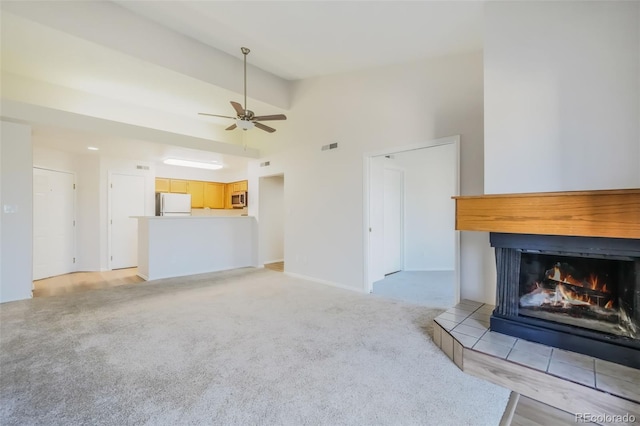 unfurnished living room with a tiled fireplace, ceiling fan, high vaulted ceiling, and light carpet