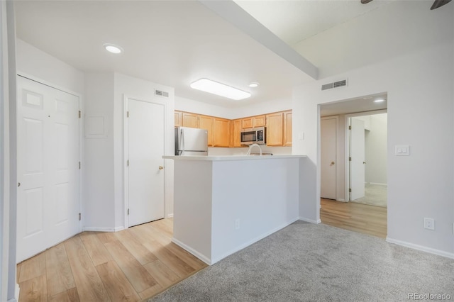 kitchen with light brown cabinets, light colored carpet, and stainless steel appliances