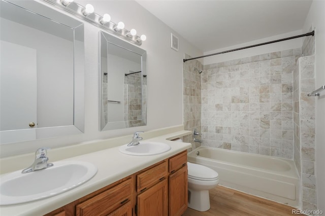 full bathroom featuring hardwood / wood-style floors, vanity, tiled shower / bath combo, and toilet