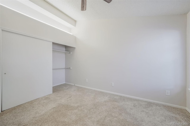 unfurnished bedroom featuring ceiling fan, a closet, light carpet, and a textured ceiling