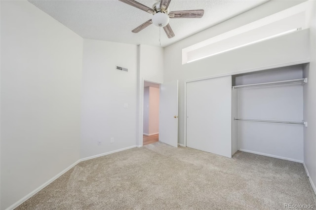 unfurnished bedroom featuring ceiling fan, light colored carpet, a high ceiling, and a closet