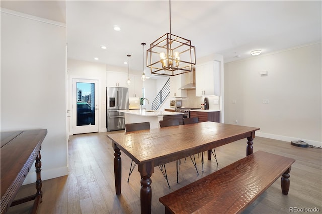 dining room featuring wood-type flooring, crown molding, a notable chandelier, and sink