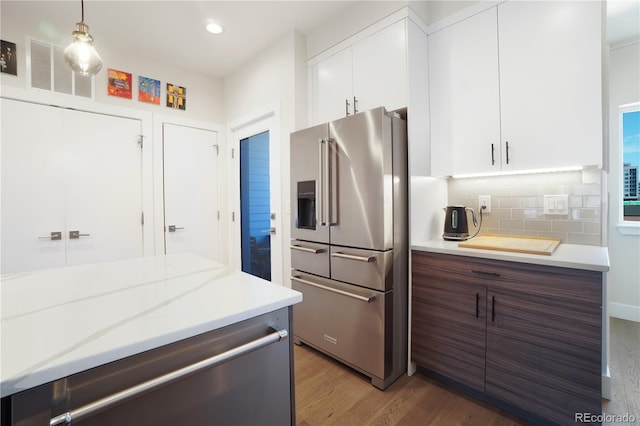 kitchen with pendant lighting, hardwood / wood-style floors, tasteful backsplash, stainless steel appliances, and white cabinets