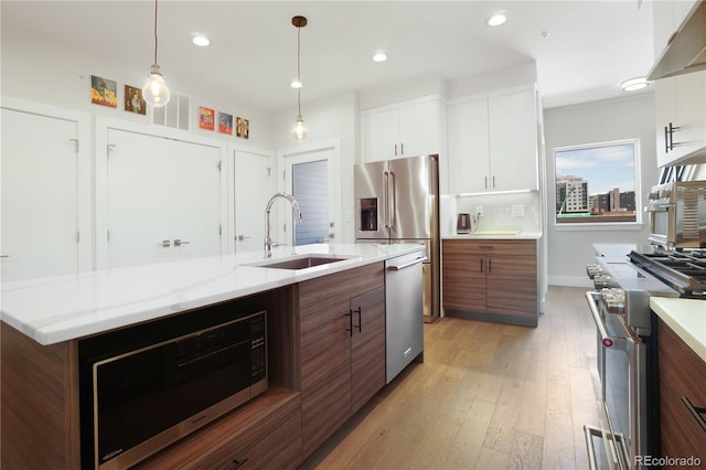 kitchen with light wood-type flooring, an island with sink, sink, appliances with stainless steel finishes, and white cabinets