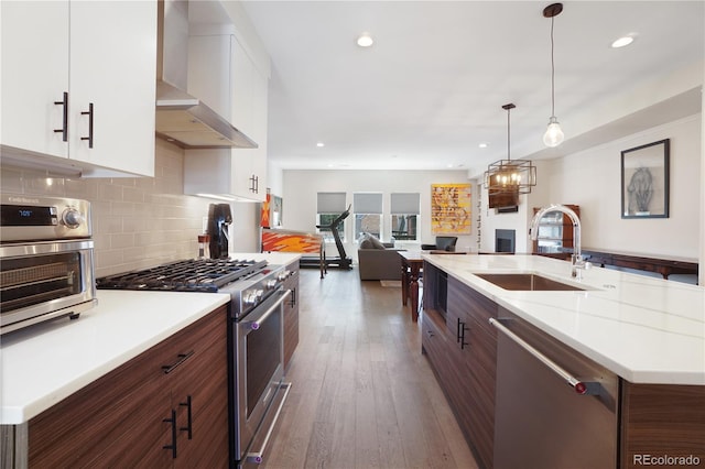 kitchen with appliances with stainless steel finishes, white cabinetry, sink, wall chimney range hood, and dark wood-type flooring