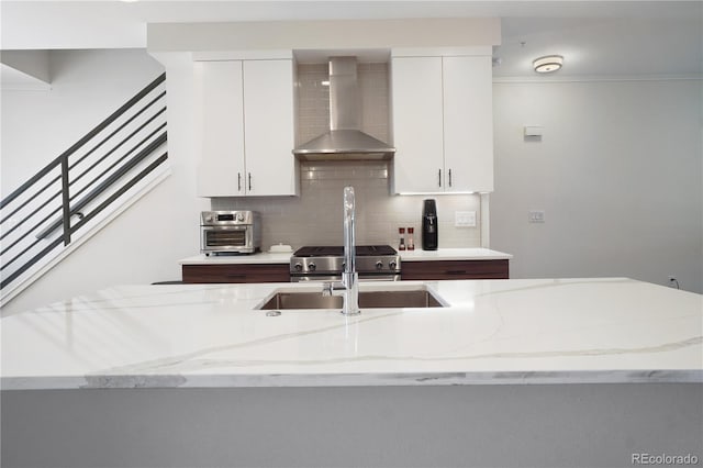 kitchen featuring wall chimney range hood, white cabinets, light stone countertops, and backsplash