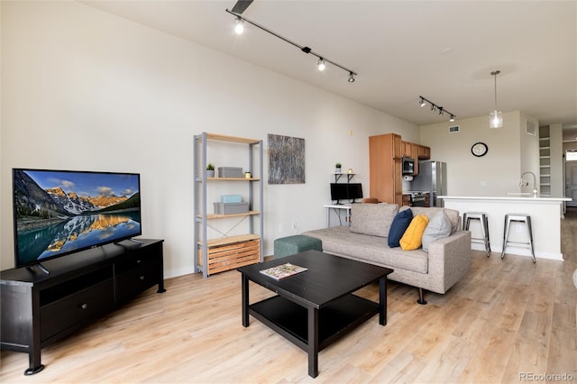 living room featuring rail lighting, light hardwood / wood-style floors, and sink