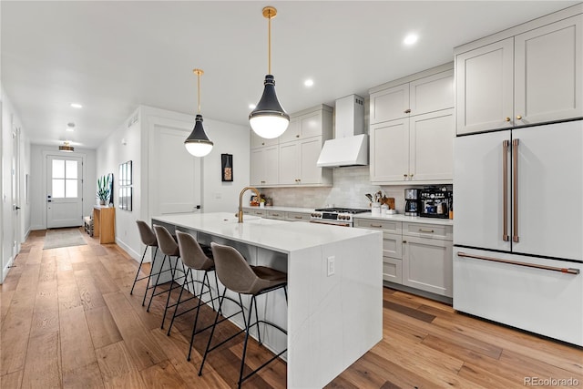 kitchen featuring a breakfast bar, high end appliances, a center island with sink, decorative light fixtures, and custom range hood