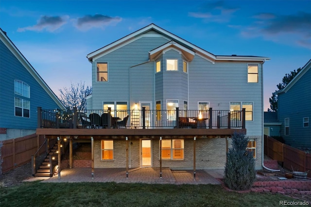 back house at dusk with a deck, a patio area, and a lawn