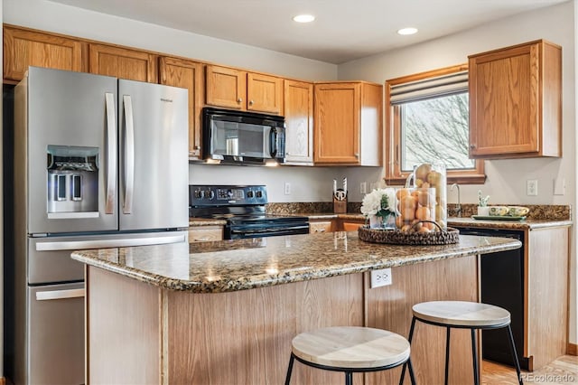 kitchen with a breakfast bar area, black appliances, dark stone counters, and a center island