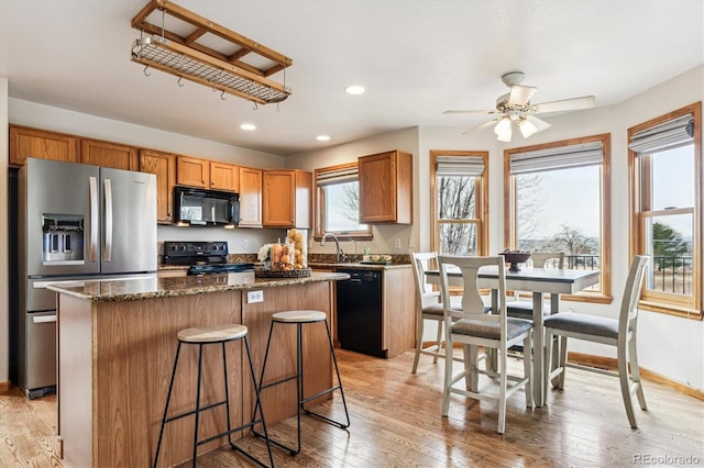 kitchen featuring dark stone countertops, light wood-type flooring, a kitchen island, and black appliances