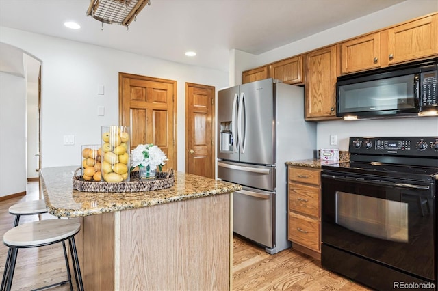 kitchen with a kitchen breakfast bar, light stone countertops, light hardwood / wood-style floors, and black appliances