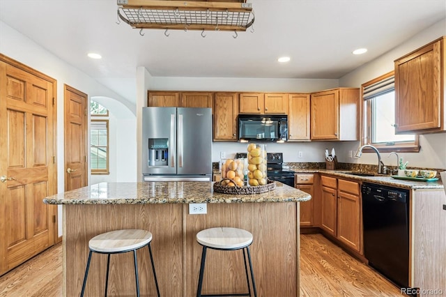 kitchen featuring sink, stone counters, a kitchen island, black appliances, and a kitchen bar