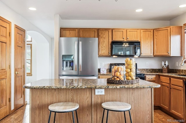 kitchen featuring stainless steel fridge, a kitchen breakfast bar, stone counters, and a kitchen island