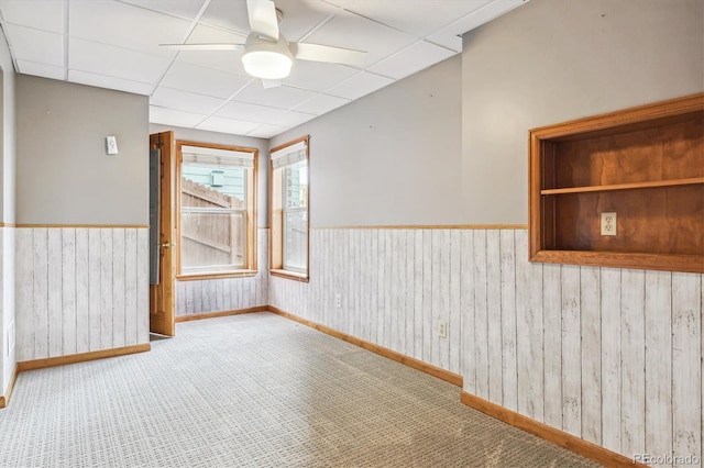 carpeted spare room featuring a paneled ceiling, ceiling fan, and wood walls