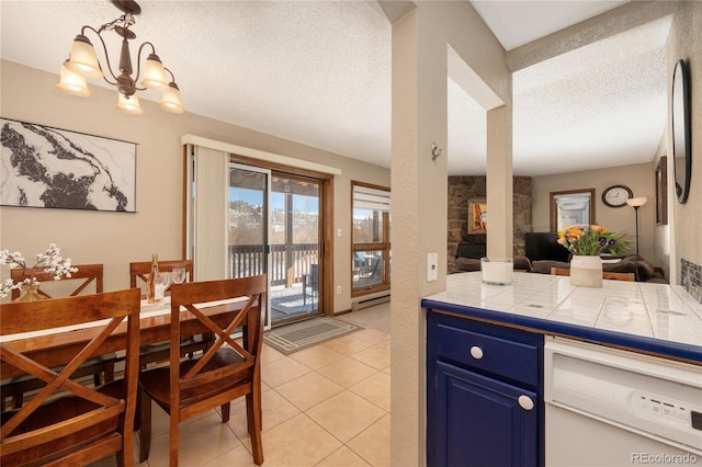 kitchen with light tile patterned floors, tile counters, blue cabinetry, dishwasher, and a textured ceiling