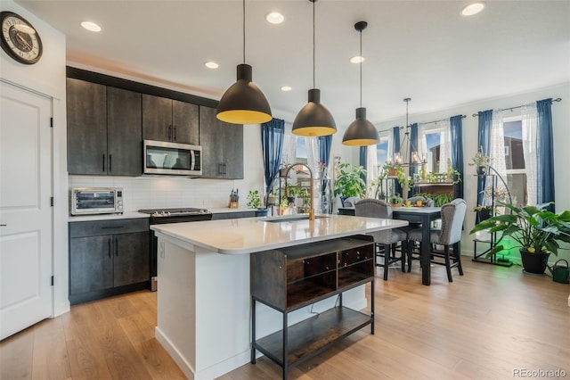 kitchen featuring an island with sink, sink, light hardwood / wood-style floors, appliances with stainless steel finishes, and decorative light fixtures