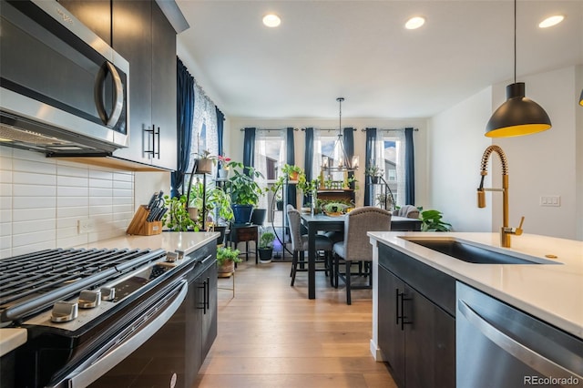 kitchen featuring hanging light fixtures, sink, appliances with stainless steel finishes, light hardwood / wood-style floors, and decorative backsplash