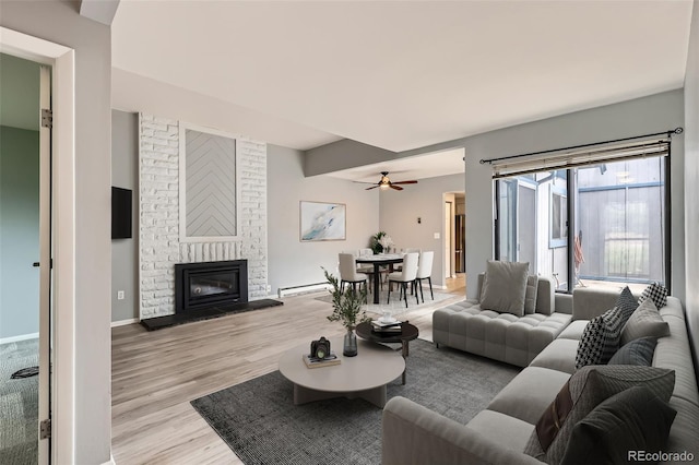 living area with baseboard heating, light wood-type flooring, a fireplace, ceiling fan, and baseboards