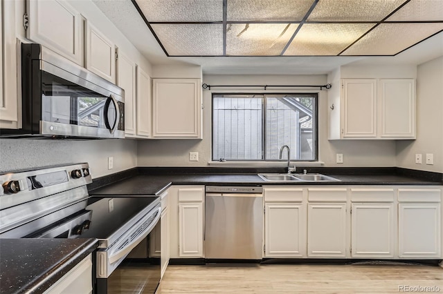 kitchen with appliances with stainless steel finishes, a sink, dark countertops, light wood finished floors, and white cabinets