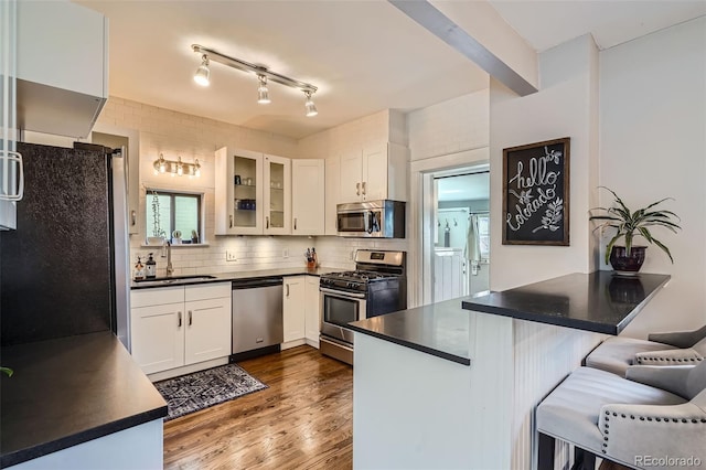 kitchen featuring a sink, a kitchen breakfast bar, appliances with stainless steel finishes, decorative backsplash, and dark countertops