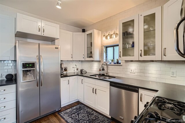 kitchen featuring dark wood-type flooring, a sink, appliances with stainless steel finishes, decorative backsplash, and dark countertops