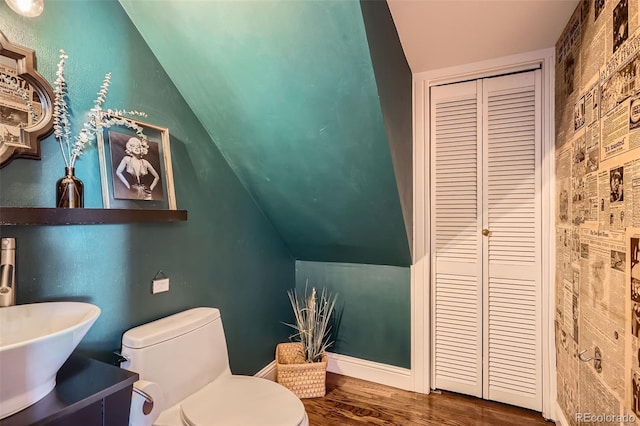 half bathroom with toilet, a sink, vaulted ceiling, wood finished floors, and baseboards