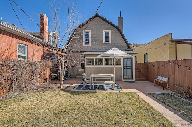 rear view of house with a yard, a patio, a chimney, a gambrel roof, and a fenced backyard