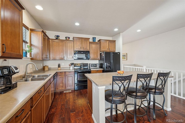 kitchen featuring dark hardwood / wood-style flooring, a breakfast bar, sink, black appliances, and a kitchen island