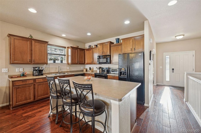 kitchen with a breakfast bar, black appliances, sink, a kitchen island, and dark hardwood / wood-style flooring