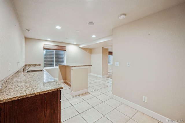 kitchen featuring kitchen peninsula, light tile patterned floors, light stone countertops, and sink