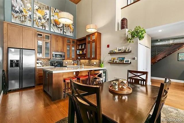 kitchen with appliances with stainless steel finishes, backsplash, a center island with sink, dark hardwood / wood-style flooring, and decorative light fixtures