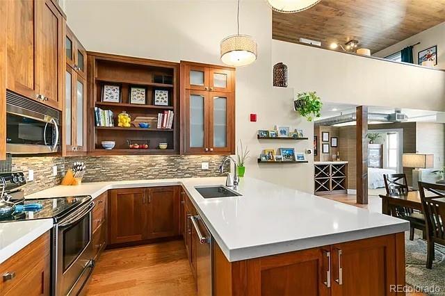 kitchen with sink, tasteful backsplash, hanging light fixtures, appliances with stainless steel finishes, and light hardwood / wood-style floors