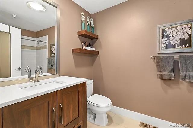 bathroom featuring tile patterned flooring, vanity, a tile shower, and toilet