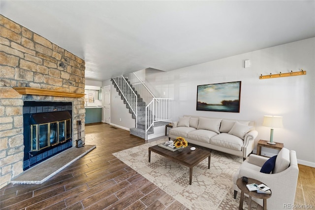 living area featuring a stone fireplace, wood finished floors, visible vents, baseboards, and stairs