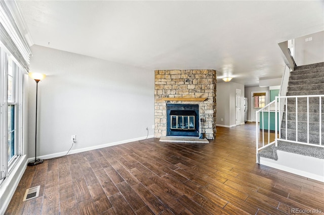 unfurnished living room featuring a stone fireplace, stairway, wood finished floors, and visible vents