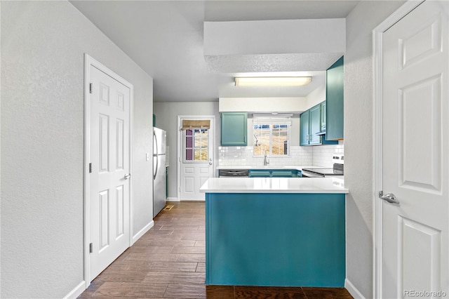 kitchen with dark wood finished floors, decorative backsplash, blue cabinets, a peninsula, and stainless steel appliances