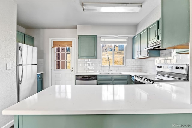 kitchen with a sink, stainless steel appliances, decorative backsplash, and green cabinetry