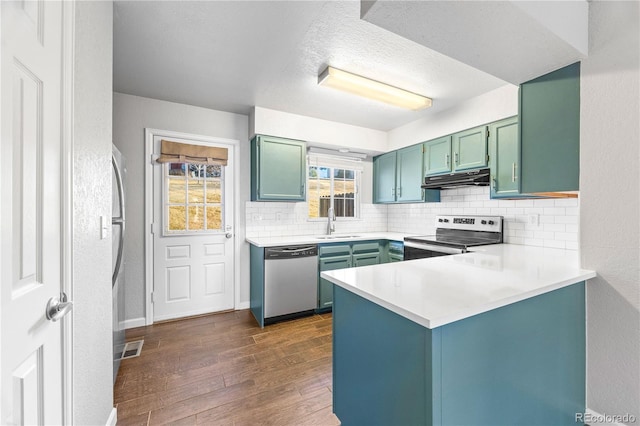 kitchen with dark wood finished floors, appliances with stainless steel finishes, a peninsula, under cabinet range hood, and backsplash